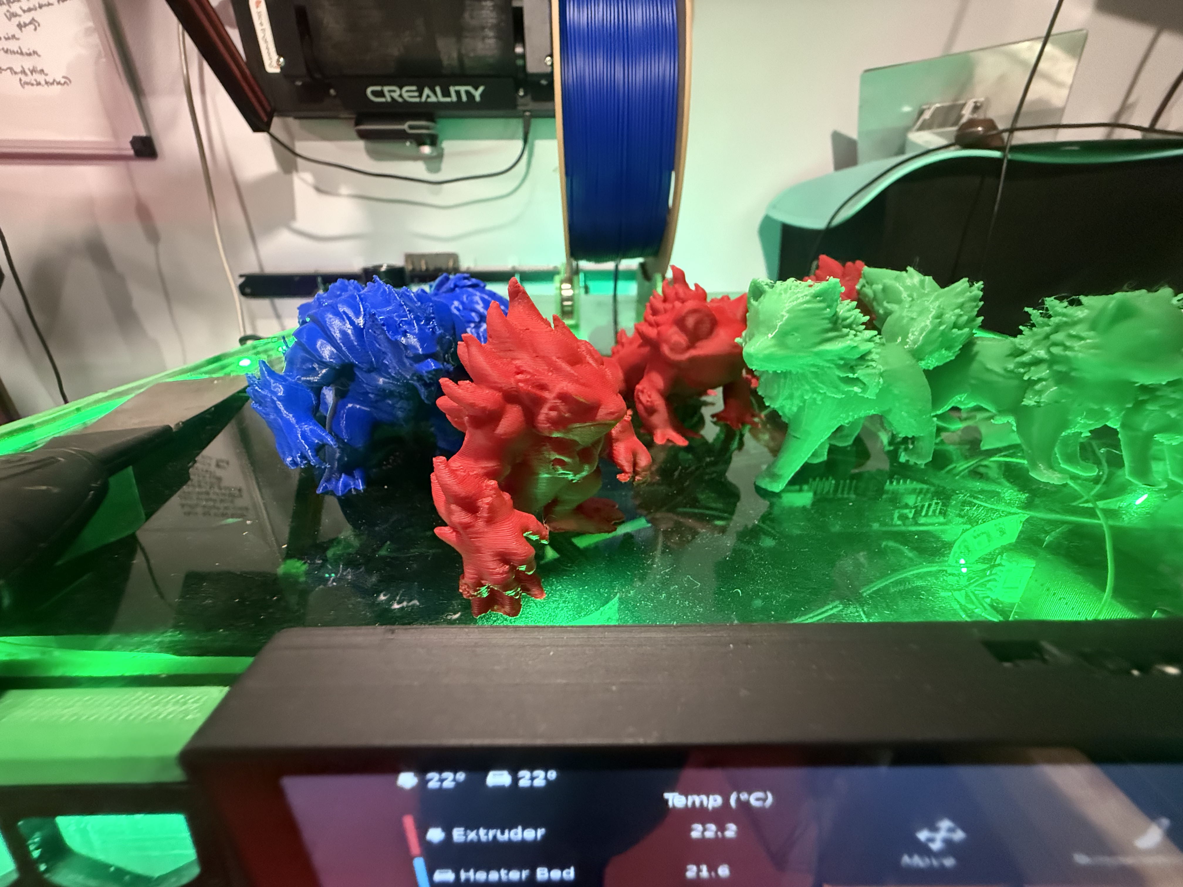 Blue, red, and green dragon models on 3D printer build plates in the DDA workshop