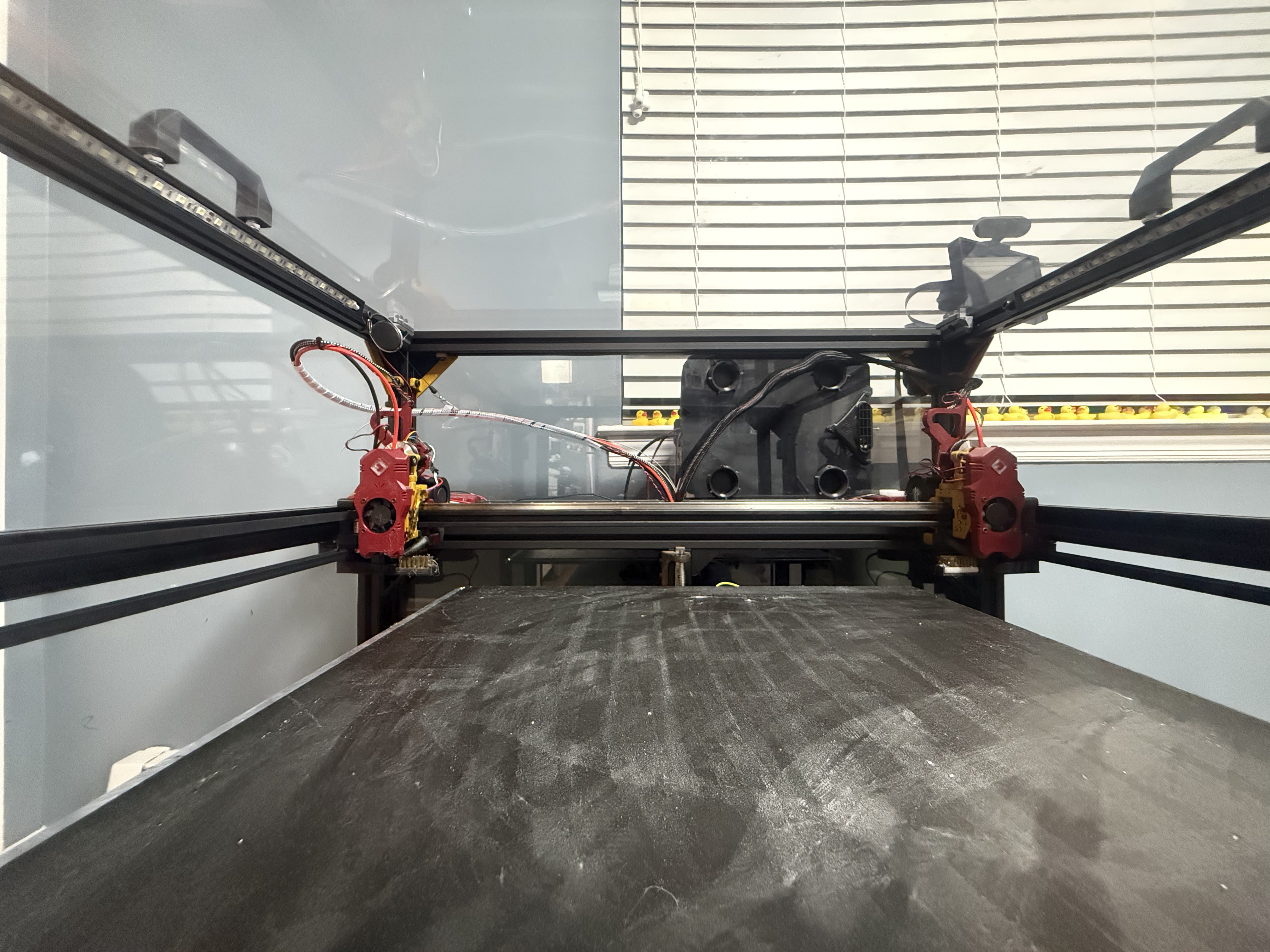 View across a large 3D printer’s build surface toward its toolhead and frame